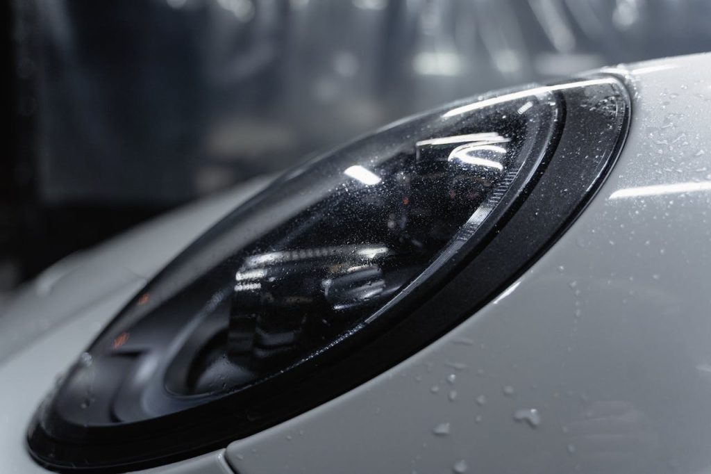 Detailed shot of a sleek car headlight with water droplets enhancing its glossy surface.